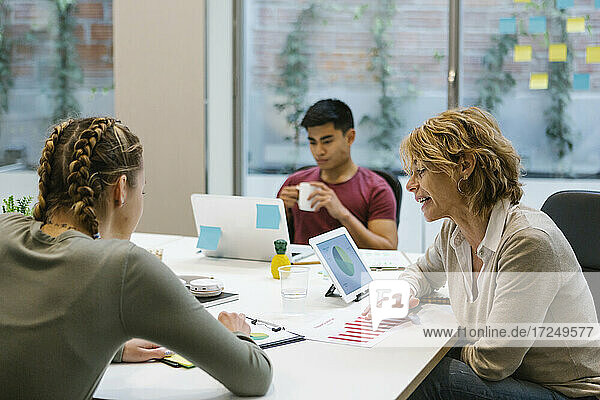 Female professionals discussing over business plan while businessman having coffee at desk
