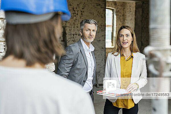 Weiblicher Kollege im Gespräch mit einem Bauarbeiter  während er neben einem männlichen Architekten steht