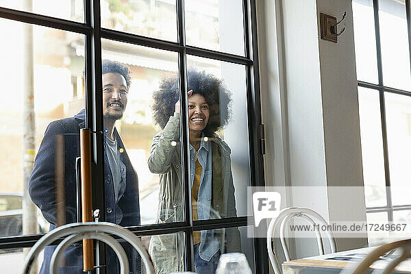 Paar schaut durch ein Glasfenster ins Innere eines Cafés