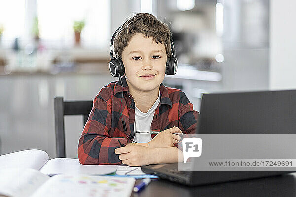 Lächelnder Junge mit Kopfhörern  der zu Hause vor einem Laptop sitzt