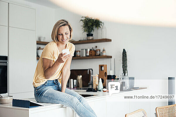 Schöne lächelnde Frau sitzt auf Küchenzeile zu Hause