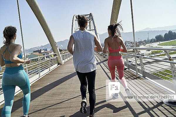 Male and female friends jogging on bridge during sunny day