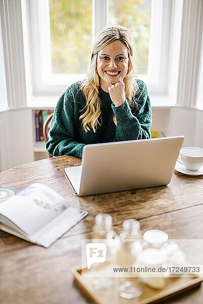 Smiling female entrepreneur sitting with laptop in office