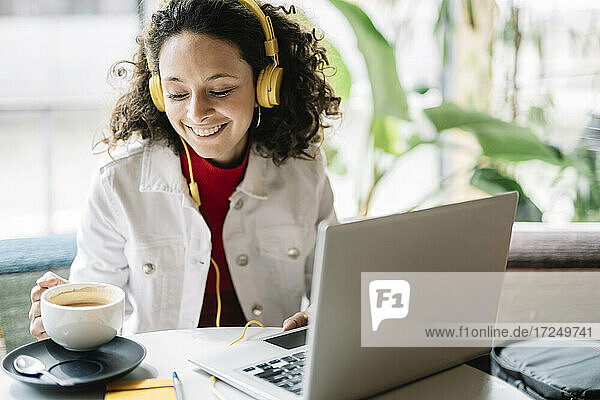 Lächelnde Frau mit Laptop und Kopfhörern bei einem Kaffee im Café