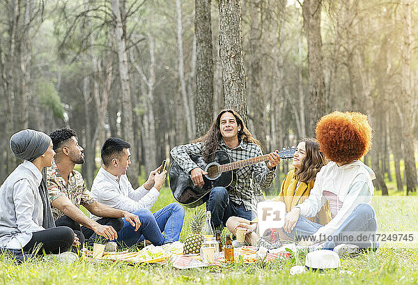 Mann mit männlichen und weiblichen Freunden spielt Gitarre beim Picknick im Wald