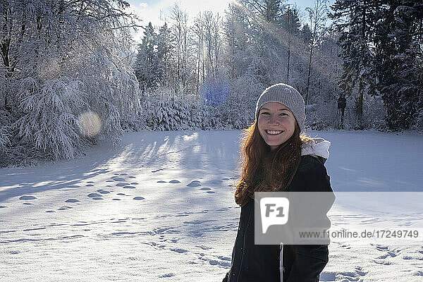 Lächelnde schöne Frau im Schnee stehend an einem sonnigen Tag