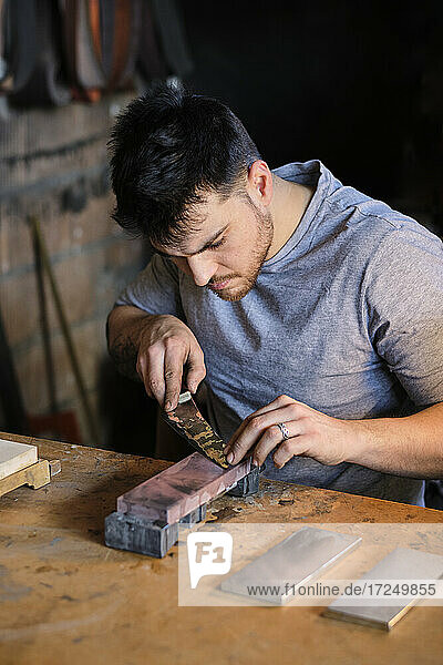 Männlicher Metallarbeiter schärft ein Messer auf einem Tisch in einer Werkstatt