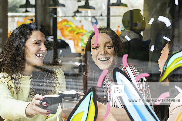 Junge Freundinnen lächelnd beim Toasten einer Kaffeetasse im Café