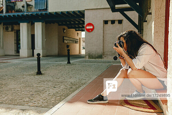 Frau  die auf dem Gehweg sitzend ein Foto durch eine Kamera macht