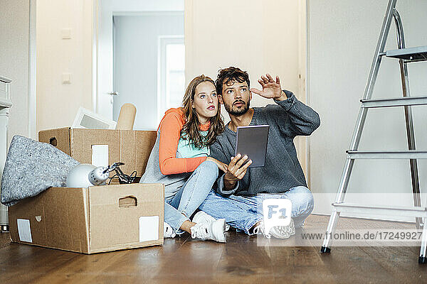 Junges Paar sitzt mit digitalem Tablet und diskutiert im neuen Haus