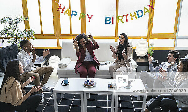 Male and female professionals clapping during birthday celebration at coworking office
