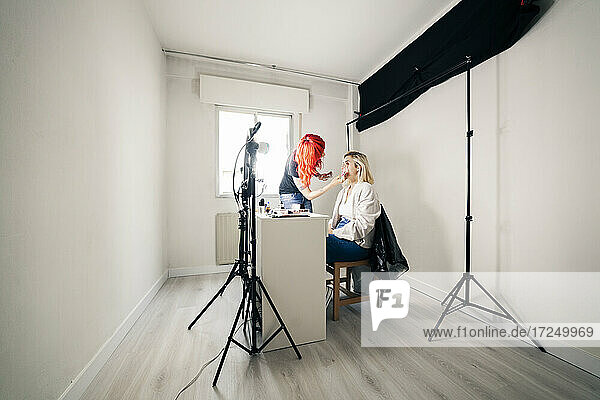 Make-up-Künstlerin trägt Gesichtspuder auf ein Modell auf  während sie im Studio bloggt
