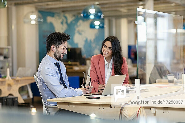 Lächelnde Geschäftsfrau  die einen männlichen Kollegen ansieht  während sie einen Geschäftsplan im Büro bespricht