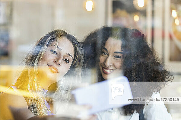 Glückliche Freundinnen  die ein Selfie mit ihrem Smartphone machen  gesehen durch ein Glas im Restaurant
