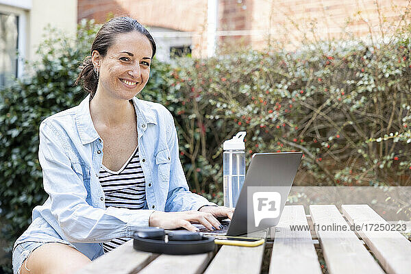 Lächelnde Unternehmerin mit Laptop im Garten