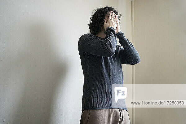 Man covering face with hands while standing at home