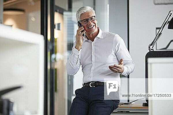 Lächelnder männlicher Unternehmer  der im Büro mit einem Mobiltelefon spricht