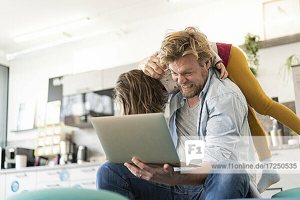 Wütender Geschäftsmann  der ein Mädchen auf der Schulter trägt  während er einen Laptop zu Hause hält