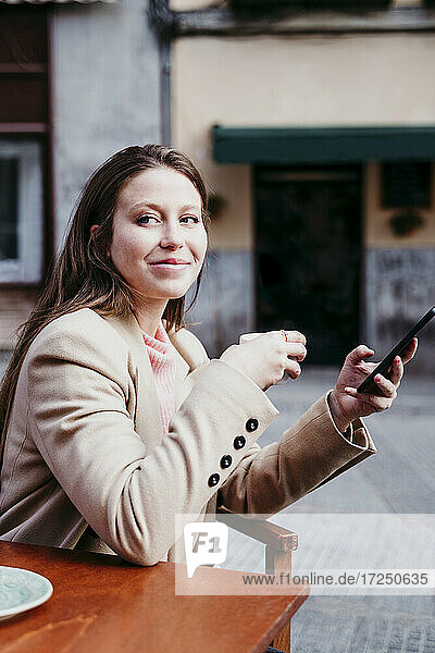 Junge Frau mit Mobiltelefon und Kaffeetasse in einem Straßencafé