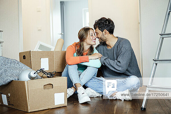 Lächelndes junges Paar sitzt zusammen bei einem Karton zu Hause
