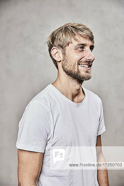 Smiling blond man looking away by wall