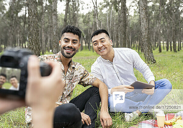 Woman photographing male friends sitting in forest during party