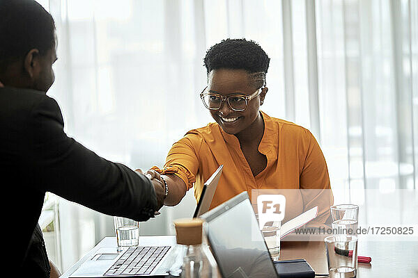 Lächelnde Geschäftsfrau schüttelt die Hand eines männlichen Mitarbeiters im Büro