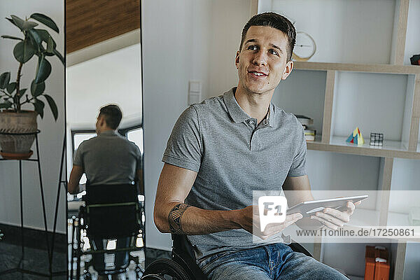 Mann mit digitalem Tablet  der auf dem Rollstuhl sitzend in einer Arztpraxis wegschaut