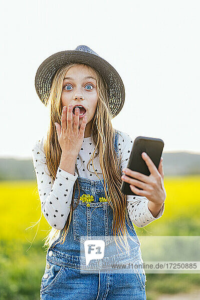 Schockiertes Mädchen mit Smartphone auf einem landwirtschaftlichen Feld