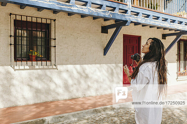 Junge Frau mit Kamera  die ein Gebäude in einem Dorf betrachtet
