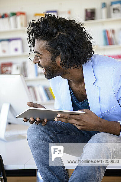 Lachender junger Mann mit digitalem Tablet in einer Bibliothek