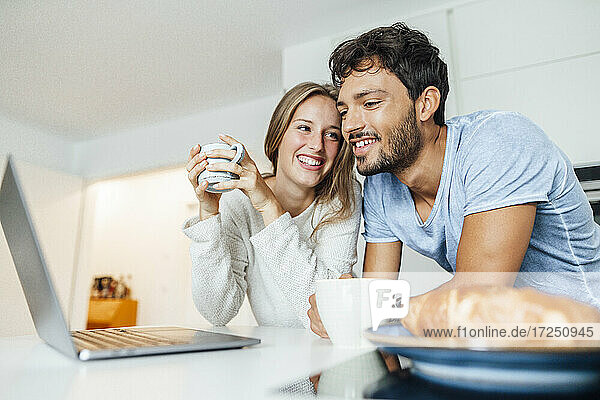 Glückliches junges Paar trinkt Kaffee und lehnt sich dabei an den Küchentisch zu Hause