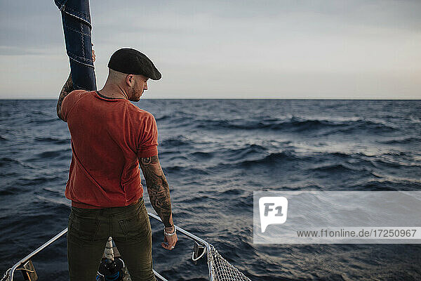 Hipster-Mann schaut weg  während er im Urlaub auf einem Boot im Meer steht