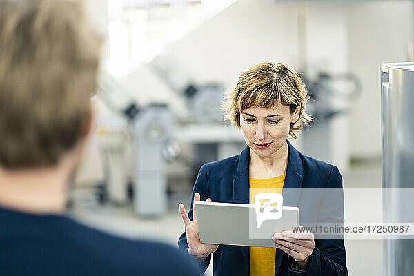 Ältere Geschäftsfrau  die ein digitales Tablet benutzt  während sie mit einem Kollegen in einer Werkstatt steht