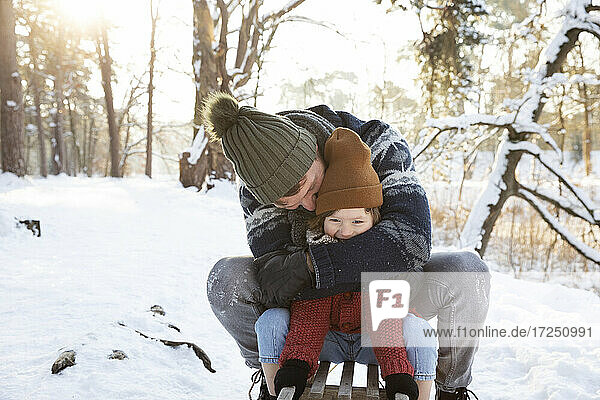 Father embracing son while sitting on sled during winter