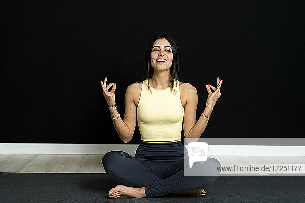 Lächelnde Sportlerin beim Üben des Lotussitzes auf einer Übungsmatte im Yogastudio