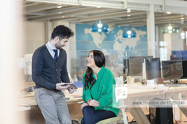 Smiling male and female entrepreneurs discussing at desk in coworking office