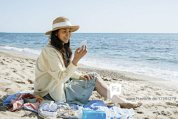 Schöne Frau benutzt ihr Smartphone  während sie am Strand im Sand sitzt