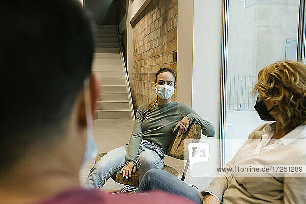Geschäftsfrau mit Gesichtsschutzmaske diskutiert mit Kollegen in der Bürolobby während COVID-19