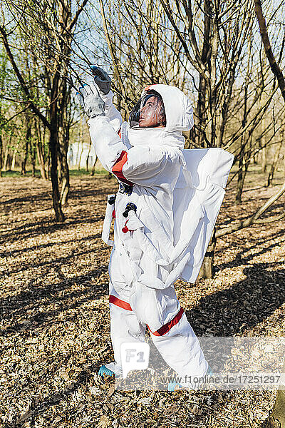 Young astronaut in space suit examining tree branch while exploring in forest