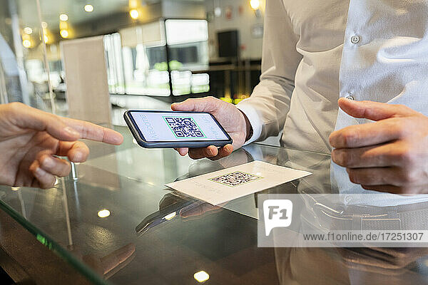 Mature man showing QR code on mobile phone at receptionist hotel desk