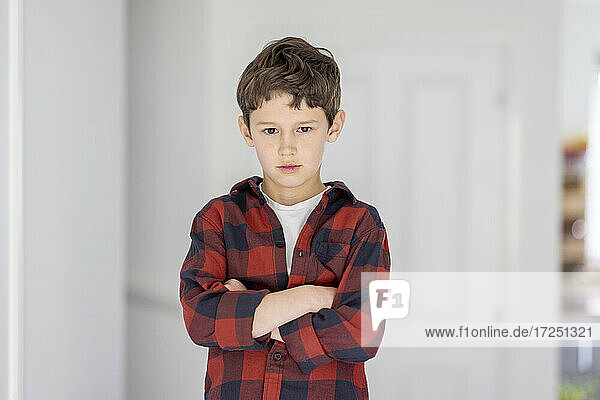 Selbstbewusster Junge mit verschränkten Armen vor einer Wand stehend
