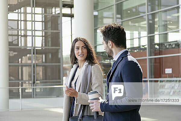 Young businesswoman holding purse while talking with colleague