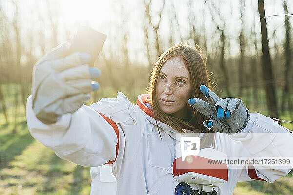 Female explorer in space suit taking selfie through mobile phone on sunny day