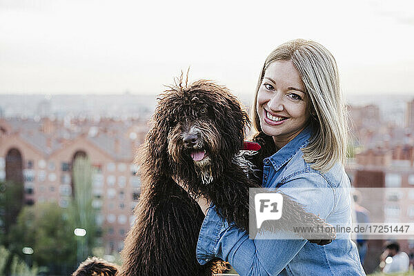 Lächelnde erwachsene Frau mit Hund vor einer Stadtlandschaft