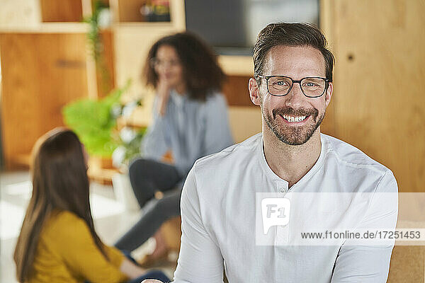 Lächelnder männlicher Unternehmer mit Kollegen im Hintergrund im Kreativbüro