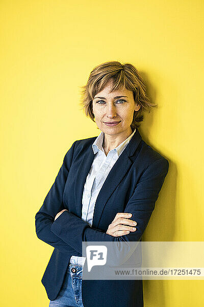 Selbstbewusste Geschäftsfrau  die sich an eine gelbe Wand lehnt