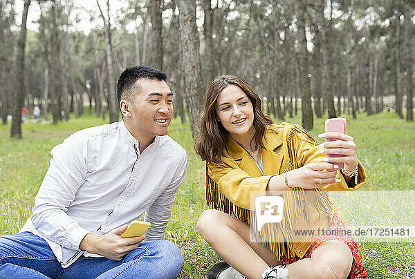 Mann mit schöner junger Frau  die ein Selfie mit ihrem Smartphone macht  während sie im Wald sitzen
