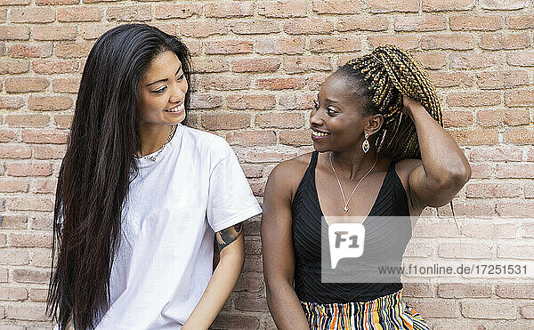 Afrikanische Frau mit Hand im Haar  die ihre Freundin an der Wand betrachtet