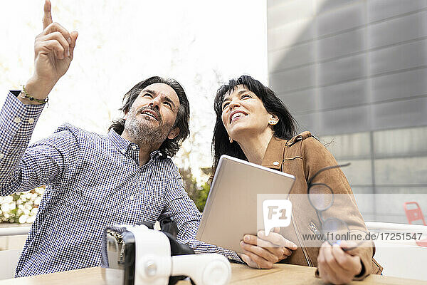Geschäftsmann mit digitalem Tablet  der auf einen Kollegen zeigt  während er auf der Terrasse sitzt